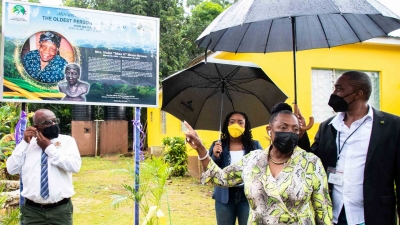 The Minister of Culture, Gender, Entertainment and Sport, the Honourable Olivia Grange, points to the storyboard erected at the home of the late supercentenarian, Mrs Violet Moss-Brown, in Duanvale, Trelwany. Mrs Moss-Brown, who lived for 117 years and 189 days, was the record holder for world’s ‘Oldest living person’. Also pictured are the Mayor of Falmouth, His Worship Councillor Colin Gager (left) and Member of Parliament for Northern Trelawny, Tova Hamilton (partially hidden) and Constable Renaldo Riley.